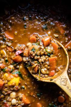 a wooden spoon full of lentils and carrots in a bowl with broth