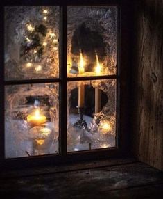 candles are lit in front of a window with frost on the windowsill and snow outside