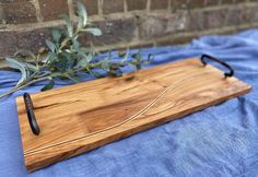 a wooden cutting board sitting on top of a blue cloth next to an olive branch