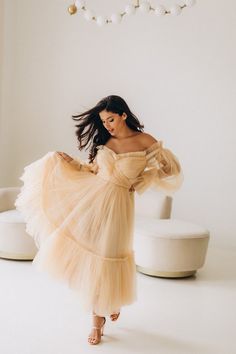 a woman in a dress is standing near a white couch and chair with her hair blowing in the wind