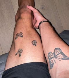 two people are holding hands with tattoos on their legs and one has a butterfly tattoo on his arm