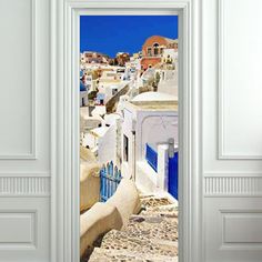 an open door leading to a white city with blue shutters and buildings in the background