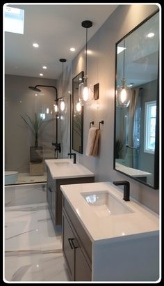 a bathroom with two sinks, mirrors and lights hanging from the ceiling in front of it