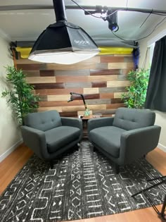 two gray chairs sitting on top of a rug in front of a wooden paneled wall