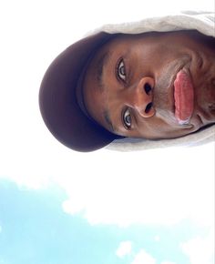 a man sticking his tongue out in front of the camera with blue sky and clouds behind him