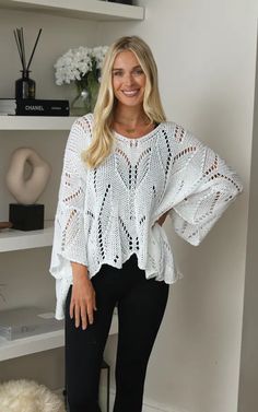 a woman standing in front of a book shelf wearing black pants and a white top