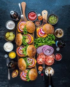 an overhead view of several sandwiches and condiments on a black surface with spoons