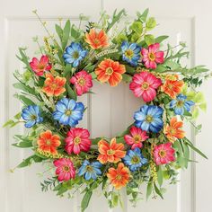 a colorful wreath is hanging on the front door with green leaves and red, blue, orange and pink flowers