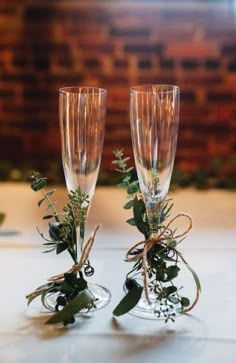 two champagne flutes with greenery in them are sitting on a table next to each other