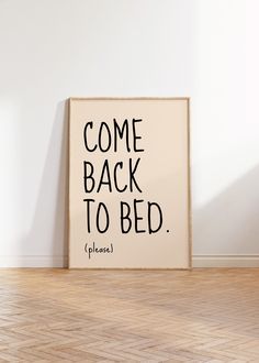 there is a sign that says come back to bed pleases on the floor in front of a white wall