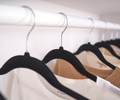 several shirts hanging on clothes racks in a row with black and white hangers next to them