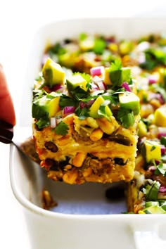 someone is cutting into a layered mexican casserole with corn and cilantro