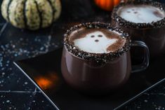 two mugs filled with hot chocolate and sprinkles on top of a black plate