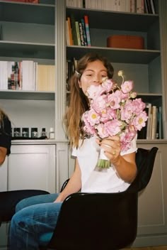 a woman sitting in a chair holding a bunch of pink flowers with her eyes closed