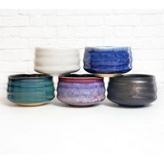 five different colored bowls sitting in front of a white brick wall and one is empty