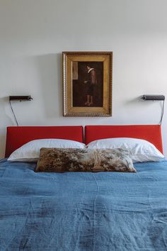 a bed with blue sheets and white pillows in front of a painting on the wall