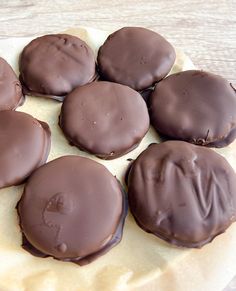 chocolate covered cookies sitting on top of a piece of wax paper next to a wooden table