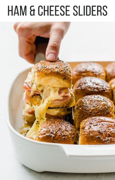 a person is taking a slider out of a casserole dish with cheese and ham