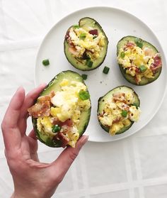 someone is holding an egg and bacon stuffed avocado halves on a white plate