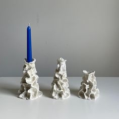 three small white vases with a blue candle in the middle one is made out of clay