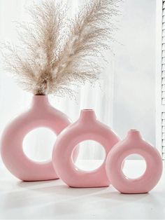 three pink vases sitting next to each other on a white counter top with dried grass in them