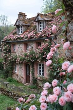 an old stone house with pink flowers growing on it