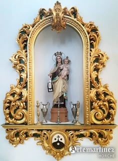 an ornate gold frame with a statue in the center and other decorations around it on a white wall