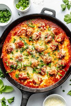 a pizza with meatballs and cheese in a skillet next to other ingredients on a white surface