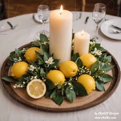 a plate with lemons, greenery and two candles on top of the table