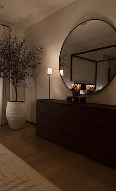 a living room with a large round mirror on the wall next to a dresser and lamp