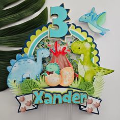 a birthday cake topper with three dinosaurs on it and the number 3 surrounded by other decorations