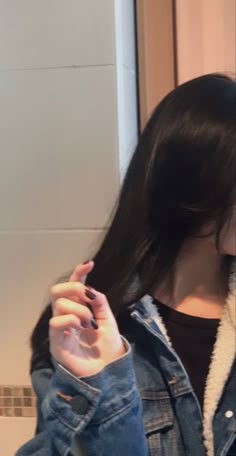 a woman with long black hair is holding her cell phone up to her ear and wearing a denim jacket