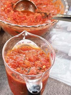 two bowls filled with tomato sauce on top of a table next to a measuring cup