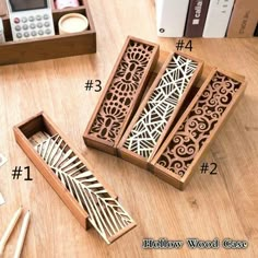 four wooden boxes with carved designs on them sitting on a table next to books and pencils