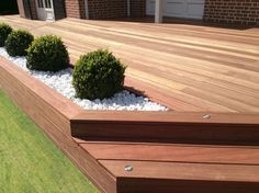 a wooden deck with white pebbles and plants in the center next to it on top of grass