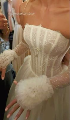 a woman in a white wedding dress is holding her hand out to the side while wearing gloves