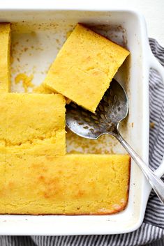 a white dish filled with cornbread next to a spoon