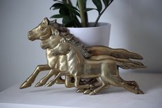 two golden horse figurines sitting next to a potted plant on a table