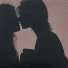 the shadow of two people kissing in front of a wall