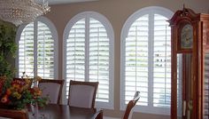 a dining room table with chairs and a grandfather clock in front of three arched windows