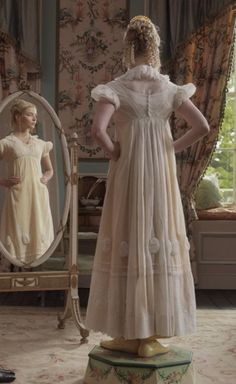 a woman standing in front of a mirror wearing a dress and looking at herself in the mirror