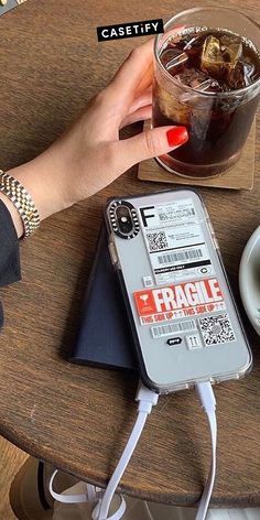 a woman is holding her cell phone while sitting at a table with a cup of coffee