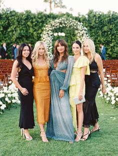 four women standing next to each other in front of an outdoor ceremony area with white flowers