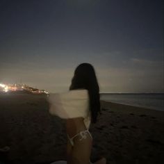 a woman sitting on top of a sandy beach next to the ocean at night time