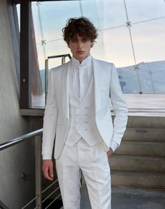 a man in a white tuxedo standing next to some stairs and looking at the camera