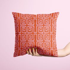 a woman holding a pillow with an orange and white pattern on the front, against a pink background