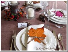 a place setting with an orange leaf on the napkin and silverware, along with pine cones