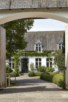 an archway leading to a white house with lots of windows and bushes on both sides