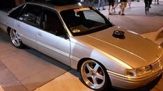 a silver car is parked on the side of the street at night with people walking by