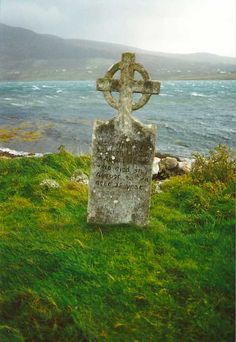 an old stone cross sitting on top of a lush green field next to the ocean